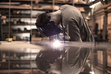 Employee welding stainless steel using welder machine - obrazy, fototapety, plakaty