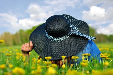 Kobieta w czarnym kapeluszu leżąca na łące wśród mleczów 