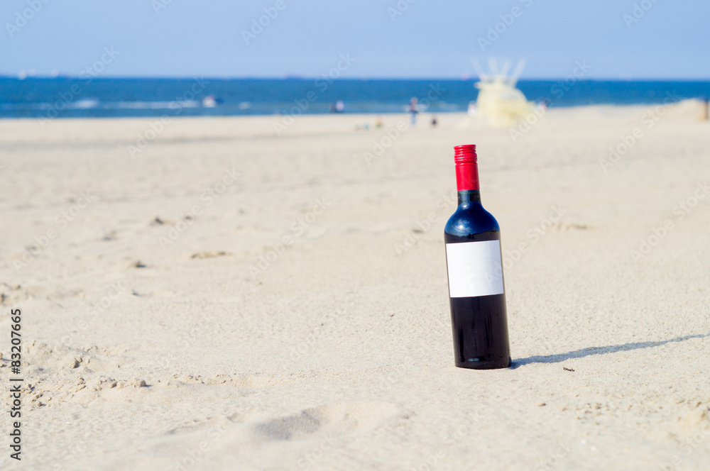 Wall mural the bottle of red wine with white label on the sunny beach