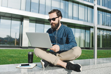 Businessman in sunglasses with laptop outdoors near of office