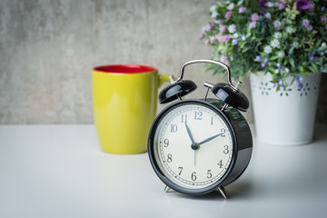 Old-time alarm clock on a white table with flowers and coffee cup