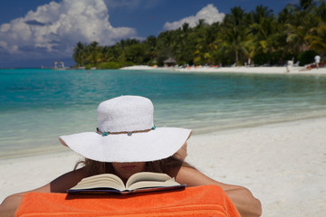 Donna con cappello  legge un libro sulla spiaggia