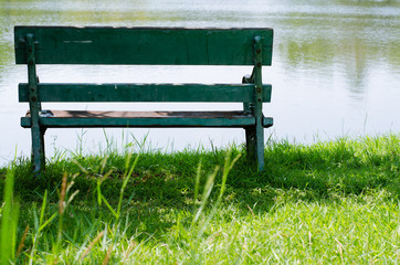Green Bench In Shade of Tree Beside Lake In Green Park.