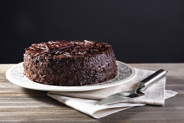 Delicious chocolate cake in plate with napkin and blade on wooden table on dark background