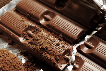 Bar of chocolate with cocoa on foil, closeup