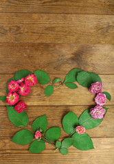 Heart of beautiful dry flowers and green leaves on wooden background