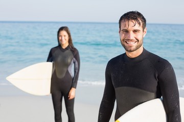 happy couple in wetsuits with surfboard on a sunny day