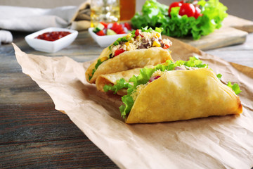 Tasty taco with vegetables on paper on table close up