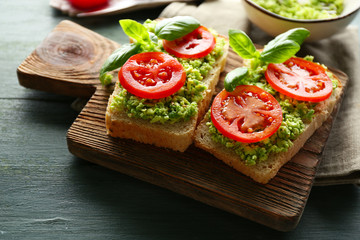 Vegan sandwich with avocado and vegetables on cutting board, on wooden background