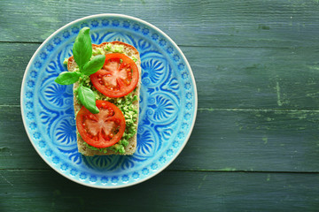 Vegan sandwich with avocado and vegetables on plate, on wooden background