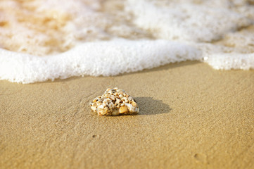 Fototapeta na wymiar Yellow rock on sand in front of foamy water wave