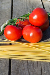 Tomatoes and pasta on a branch on rough wooden board.