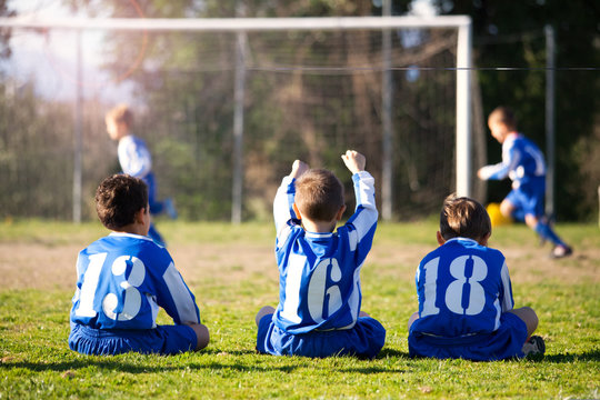 young boys in uniform watching their team while playing football