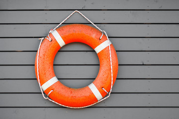 Red lifebuoy hanging on gray wooden wall