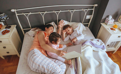 Mother reading book to her sons in the bed