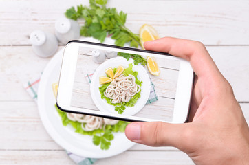 Hands taking photo squids & lemon  with smartphone.