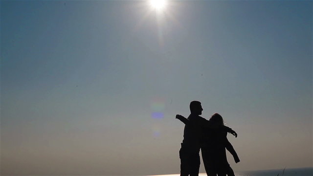 Silhouette of happy young couple embracing on a background of sky and sea. Man twirling his woman around on his hands