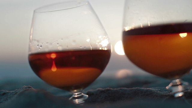 Macro extra close up of two glasses of brandy on the sand over incredible beach sunset background view