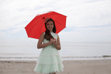 Niña con paraguas rojo y vestido verde en la playa