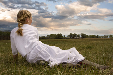 Girl wearing a dress sitting in a pasture