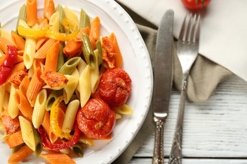 Pasta salad with pepper, carrot and tomatoes on wooden table background
