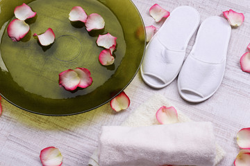 Obraz na płótnie Canvas Spa bowl with water, rose petals, towel and slippers on light background. Concept of pedicure or natural spa treatment
