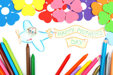Happy Mothers Day message written on paper with pencils and decorative flowers close up