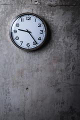 Round wall clock hanging on the grey concrete wall