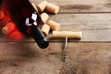 Glass bottle of wine with corks and corkscrew on wooden table background