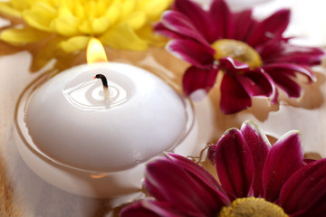 Bowl of spa water with flowers and candle, closeup