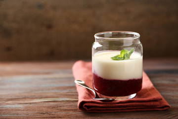 Glass jar with tasty panna cotta dessert on plate, on wooden table
