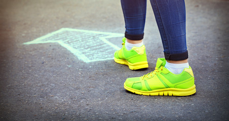 Female feet and drawing arrow on pavement background