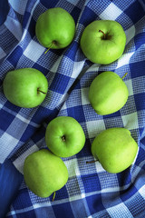 Green apples in bowl with fabric on wooden table, top view