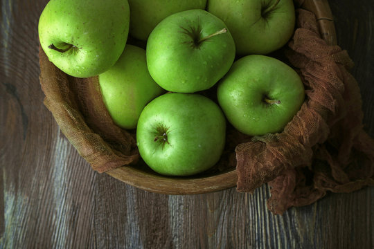 Green apples in bowl with fabric on wooden table, top view