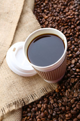Paper cup of coffee with beans on sackcloth close up