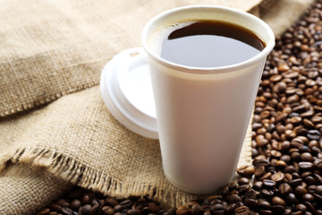 Paper cup of coffee with beans on sackcloth close up