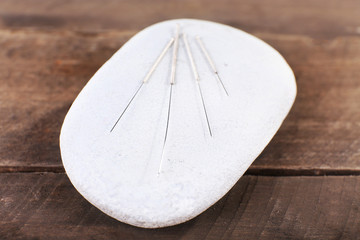 Acupuncture needles on wooden table with spa stones, closeup