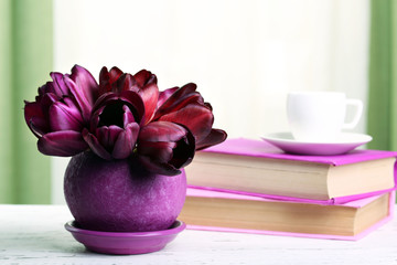 Beautiful tulips in pot with books on fabric background