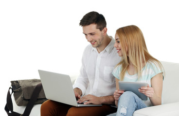 Portrait of young happy couple with baggage, digital tablet and laptop sitting on sofa. Isolated on white