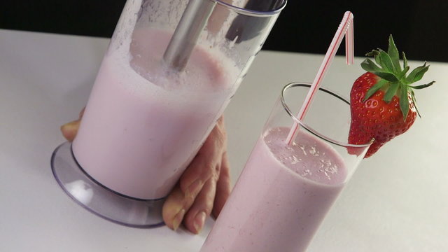 Making milk strawberry smoothie drink using stick hand blender