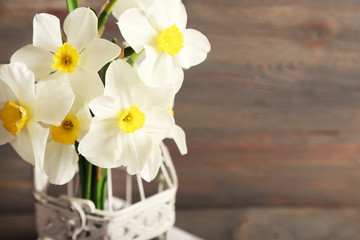 Fresh narcissus in decorative cage on wooden background