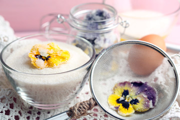 Candied sugared violet flowers, glass bowl with sugar,sieve on wooden background