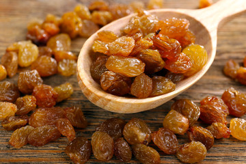 Raisins in spoon on wooden table, closeup