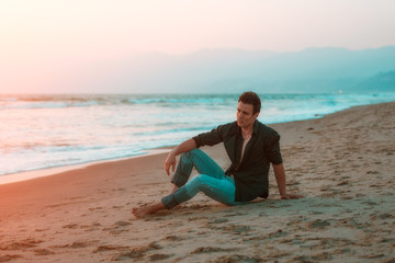 Stylish sexy and sad man sitting at beach.