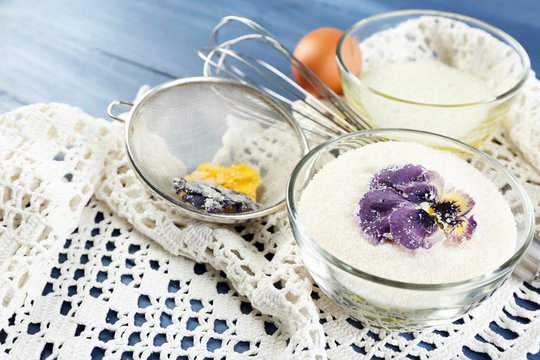 Making candied violet flowers with egg whites and sugar, on color wooden background