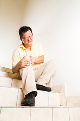 Matured man suffering acute knee joint pain seated on stairs 