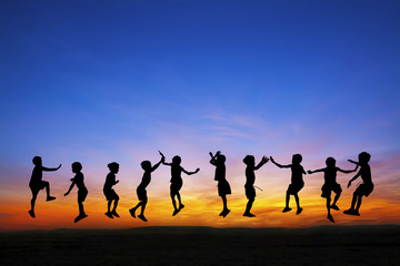 Silhouette of happy childrens jumping at sunset time
