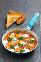 fried quail eggs in tomato sauce with toasts in a frying pan