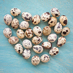 Quail eggs in shape of heart on a blue wooden background, top vi