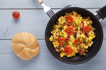 Scrambled eggs in a pan with bacon, onion and tomatoes sprinkled